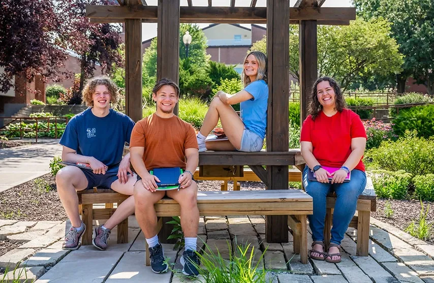 Four students sitting outside at a wooden patio. They smile at the camera.